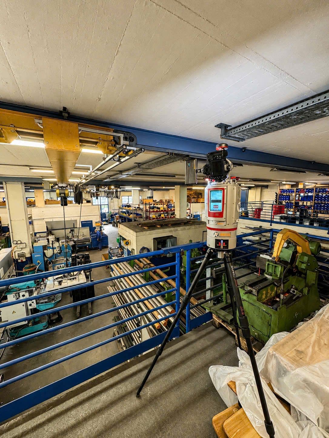 Laserscanner auf Stativ in Industriehalle, Vermessung und 3D‑Scanning einer Produktionsanlage mit Maschinen, Kranbahn und Werkstattbereich.