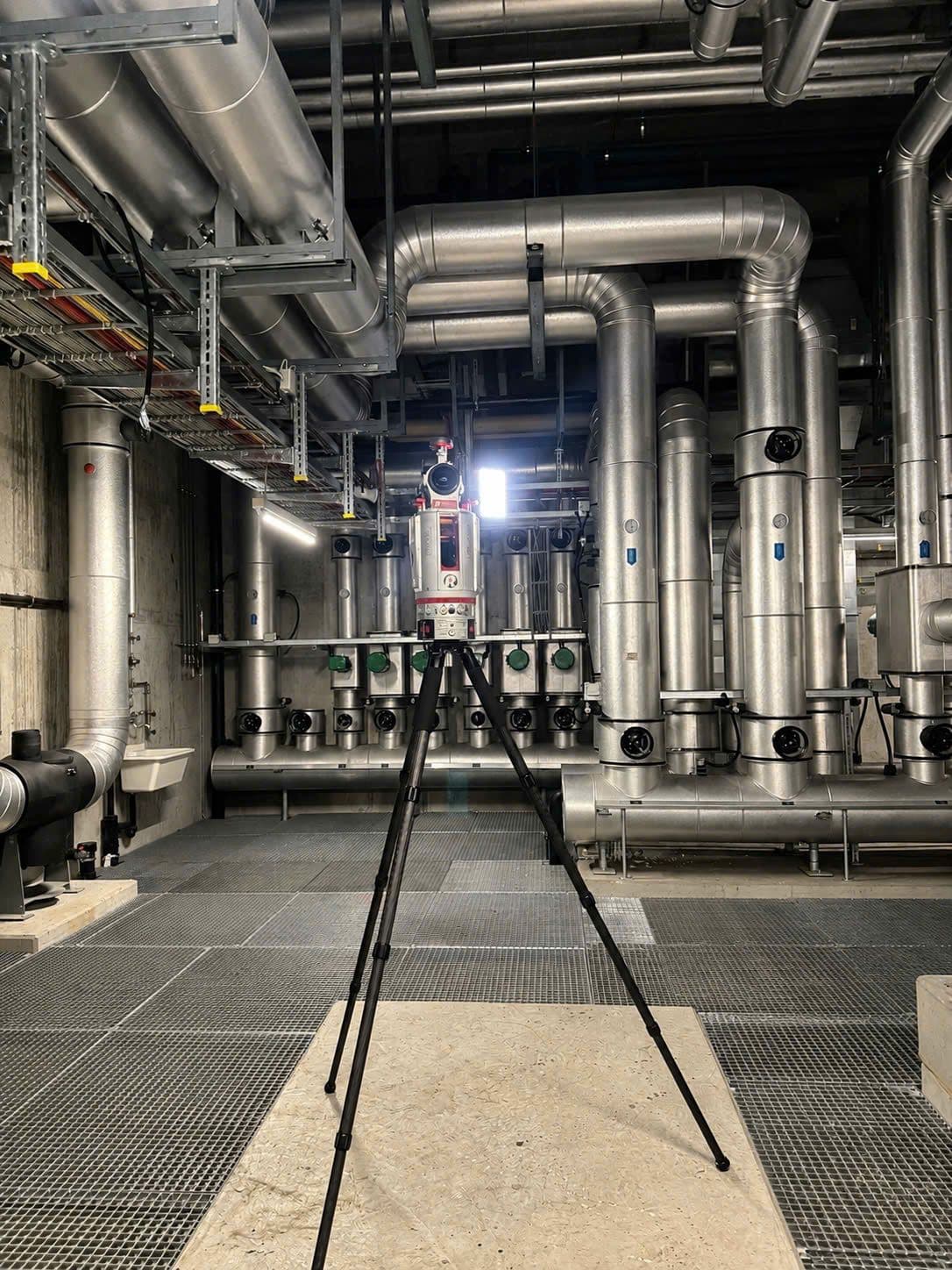 3D-Laserscanner auf Stativ in einem Technikraum mit großen Lüftungs- und Rohrleitungen; Aufnahme zur Vermessung und Dokumentation von Gebäudetechnik.