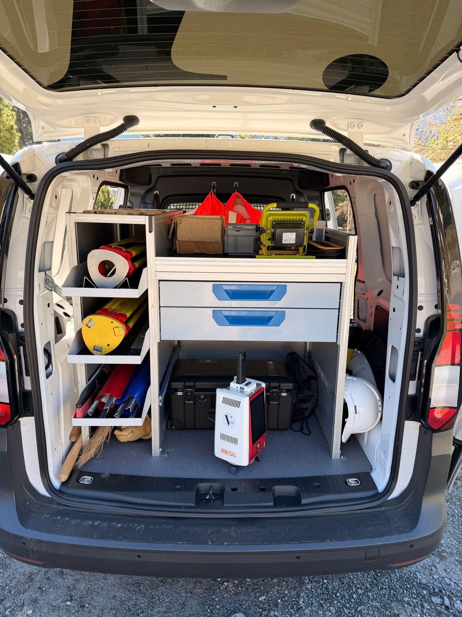 Offener Kofferraum eines Service-Transporters mit Werkstatteinrichtung: Regale, Schubladen und Werkzeugkisten, darunter Kabeltrommel, Bohrer und Zubehör – übersichtlich sortiert für Handwerker im Einsatz.