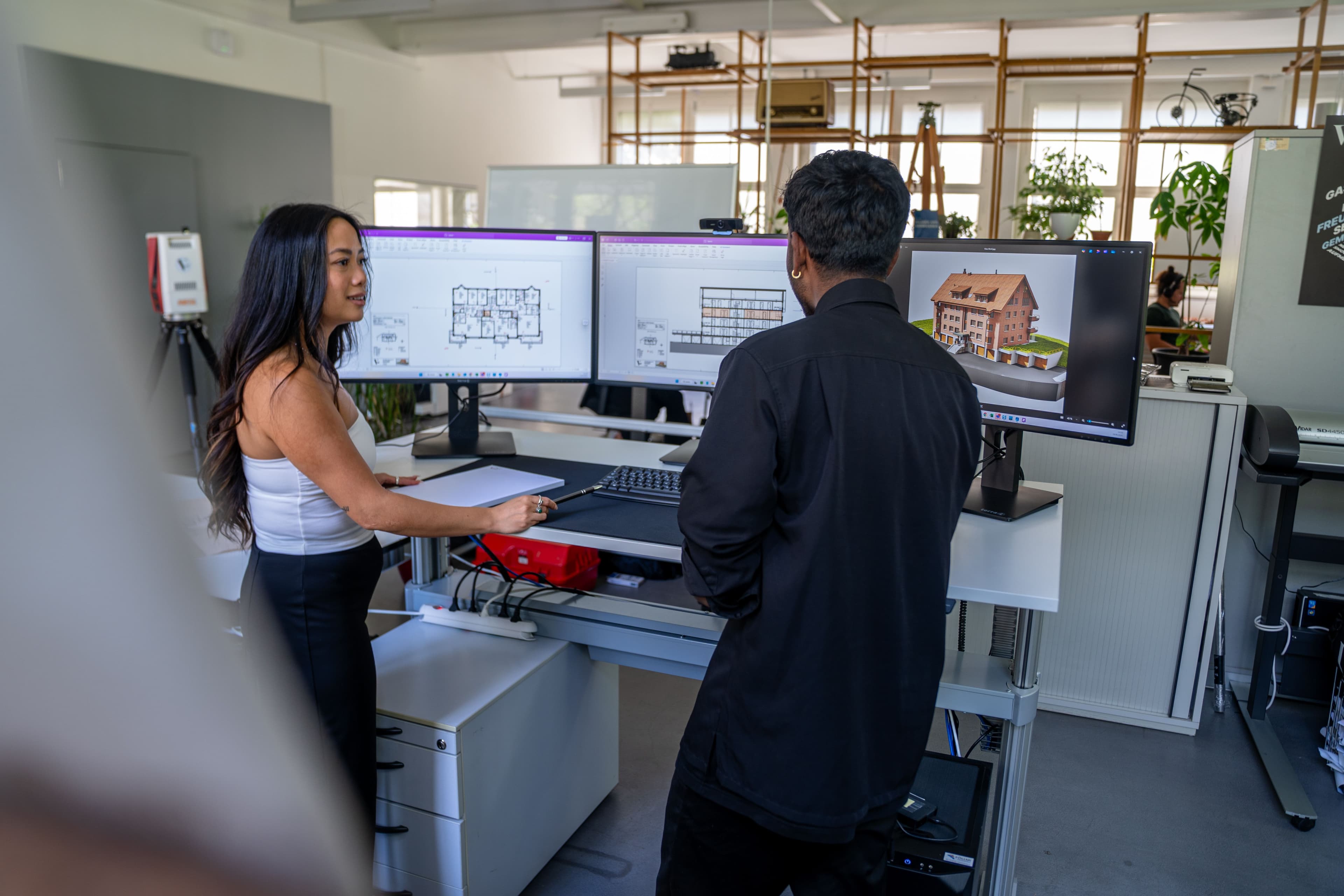 Büro mit zwei Personen, die an Schreibtischen mit mehreren Monitoren CAD-Software nutzen.