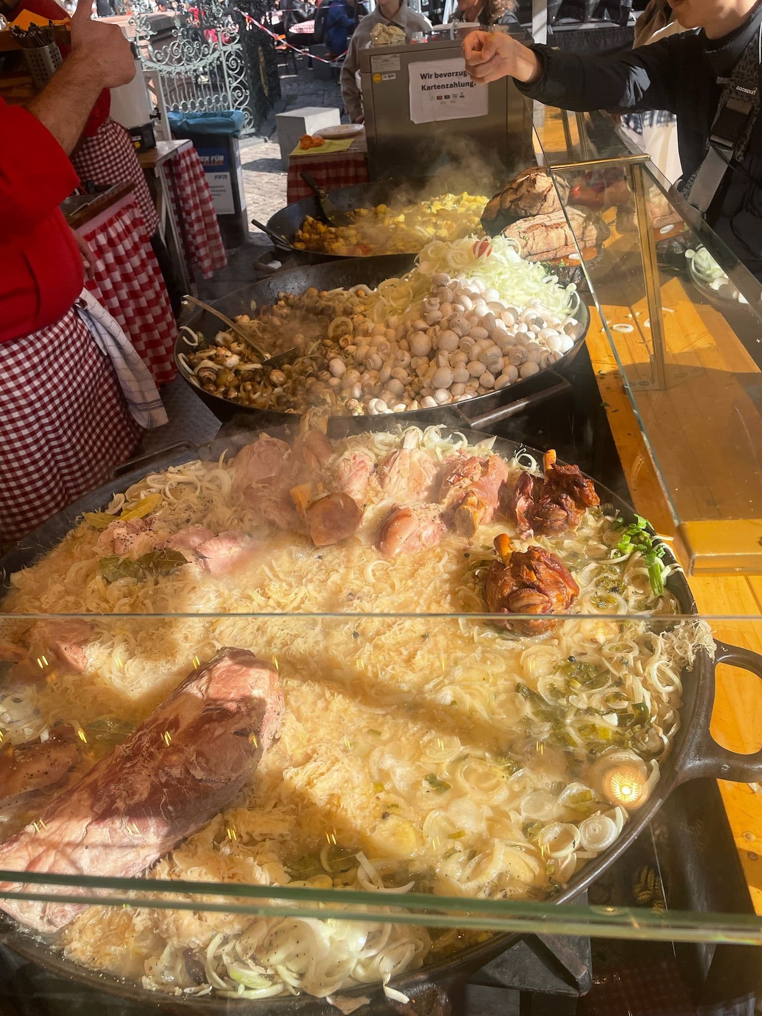 Große Pfannen mit gebratenem Sauerkraut, Fleisch und Pilzen auf einem Marktstand im Freien.