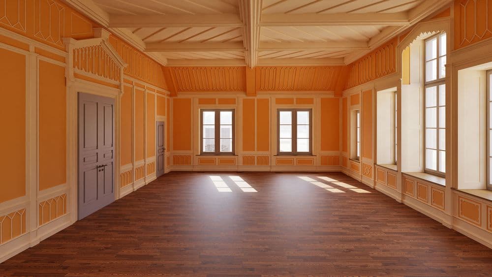 Leerer historischer Saal mit orangefarbenen Wänden, Stuckdetails, hohen Fenstern und Holzboden; Sonnenlicht fällt durch die Fenster in den Raum.