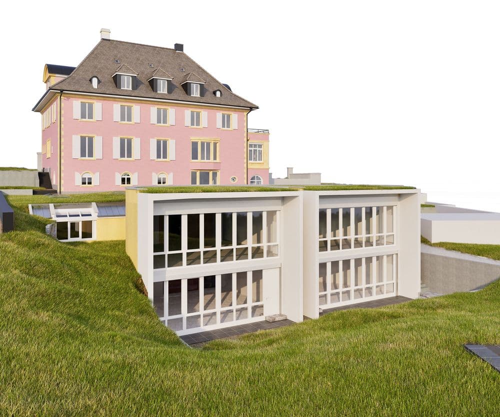 Altes rosa Haus auf Hügel mit modernen, weißen Anbauten und großen Fenstern, umgeben von grünem Rasen.
