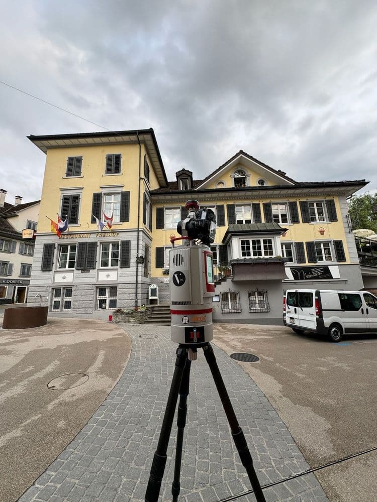 Gerät auf Stativ vor historischem Gebäude, bewölkter Himmel.