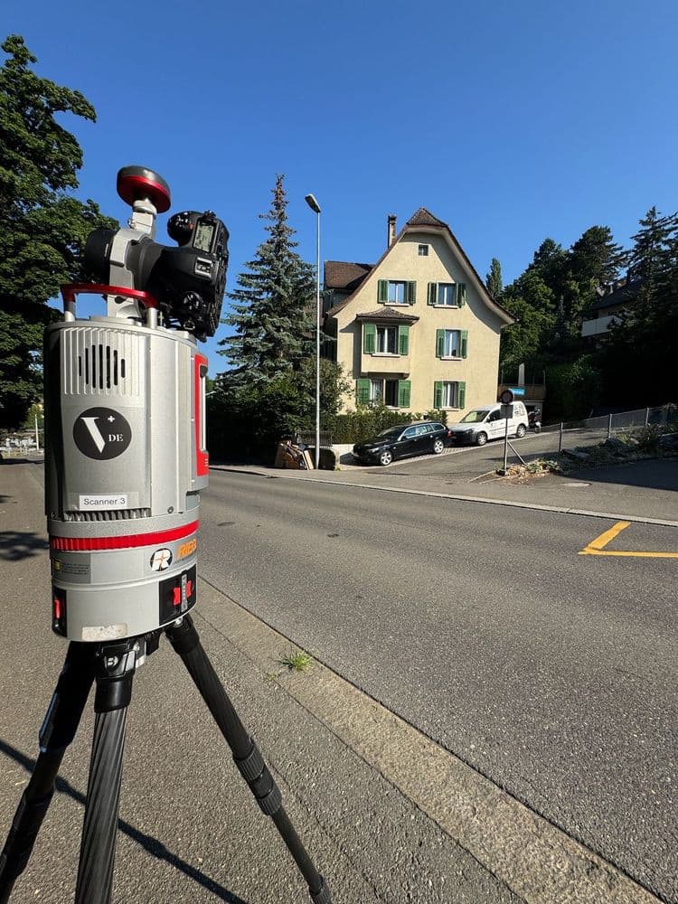 Straßenvermessung mit 3D-Laserscanner auf Stativ vor einem Haus an einer Kreuzung.