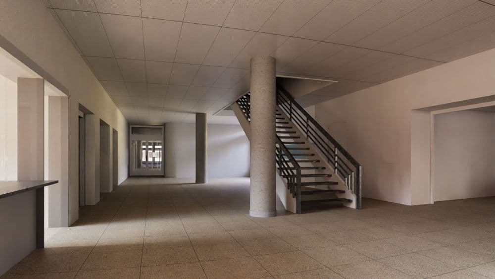 Innenansicht eines modernen Gebäudeflurs mit gefliester Bodenfläche, Betonstütze und Treppenaufgang, helle Wände und Decke, Türen und Durchgänge entlang des Korridors, Tageslicht von links.
