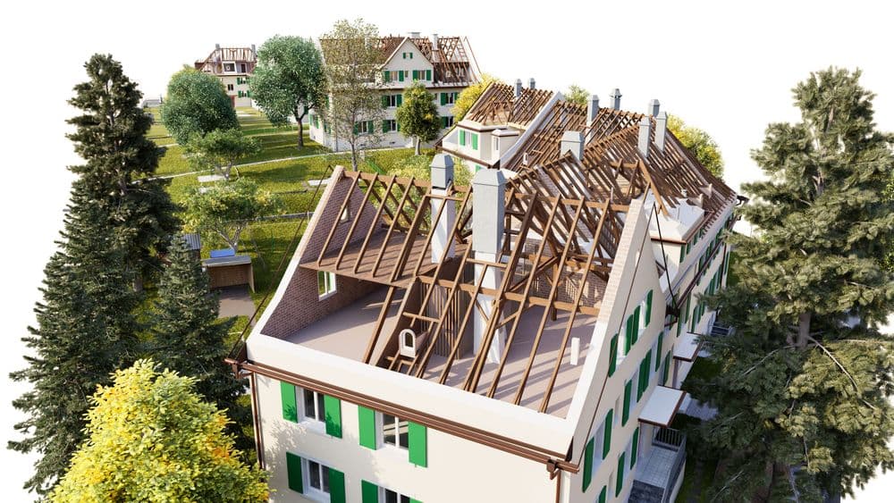 Luftaufnahme einer Wohnanlage im Grünen: Mehrfamilienhäuser mit grün-weißen Fassaden, teils freigelegtem Dachstuhl und laufender Dachsanierung, umgeben von Bäumen und Gärten.