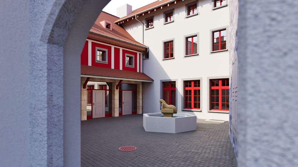 Innenhof eines historischen Gebäudekomplexes mit roten Fensterrahmen, gepflastertem Platz und Skulptur auf Sockel, Blick durch einen Torbogen bei Tageslicht.
