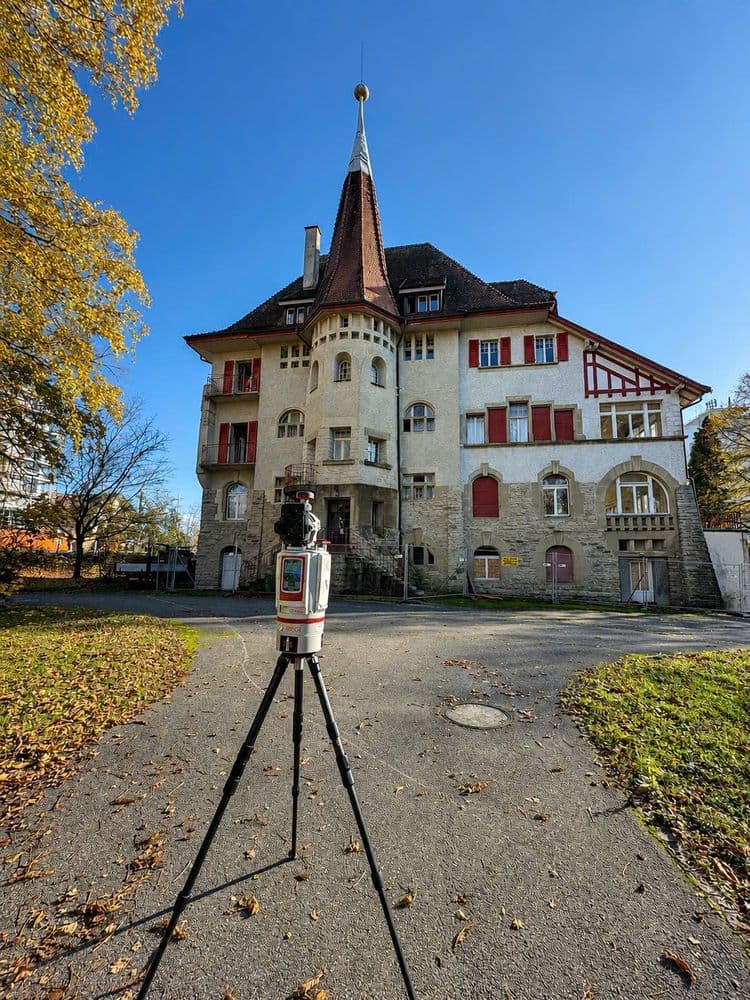Historisches Schlossgebäude mit Turm und roten Fensterläden an einem sonnigen Herbsttag; im Vordergrund steht ein Laserscanner auf Stativ im Hof, blauer Himmel und Laubbäume.