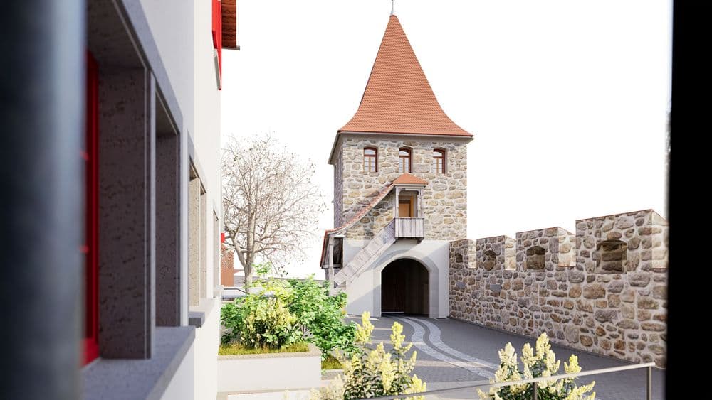Steinerner Torturm mit rotem Spitzdach und Bogenportal, umgeben von Stadtmauer; gepflasterter Weg mit Pflanzenbeeten und modernem Gebäude links bei Tageslicht.