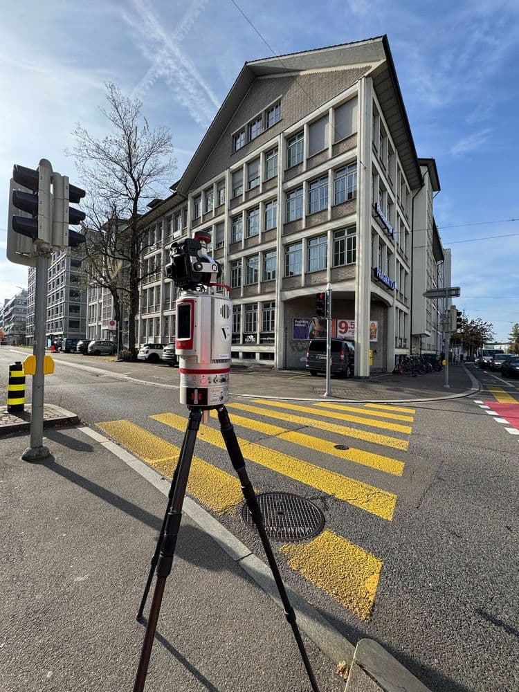 Verkehrsmessgerät auf Stativ an einer Kreuzung in einer städtischen Umgebung vor einem großen Gebäude.
