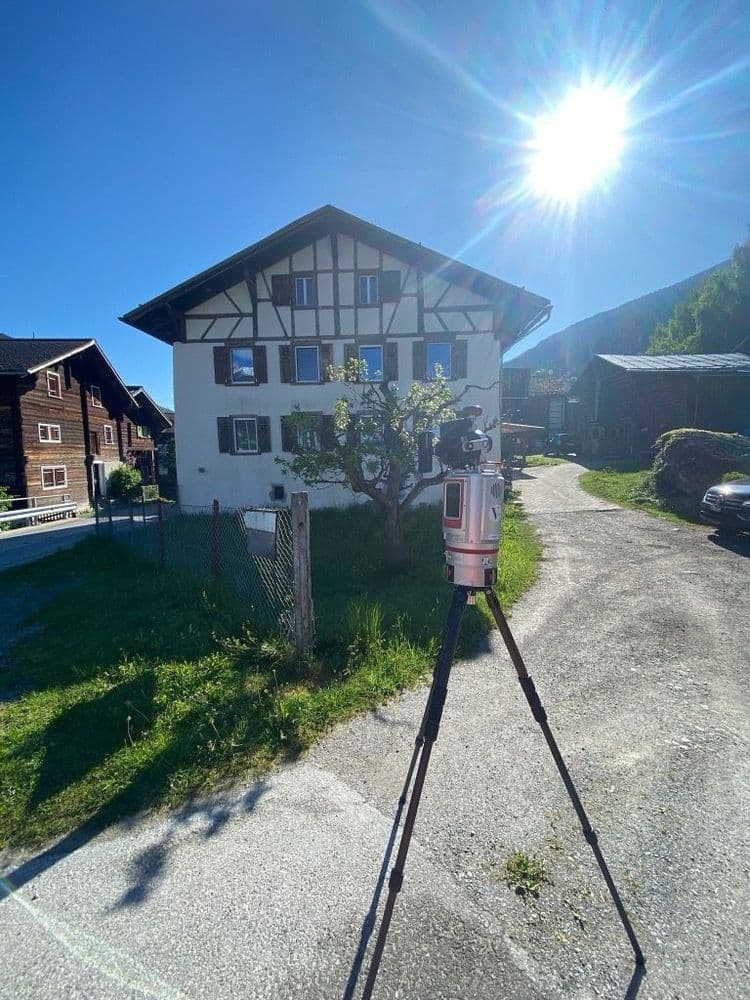 Einfamilienhaus im Sonnenschein, Vordergrund Vermessungsgerät auf Stativ.