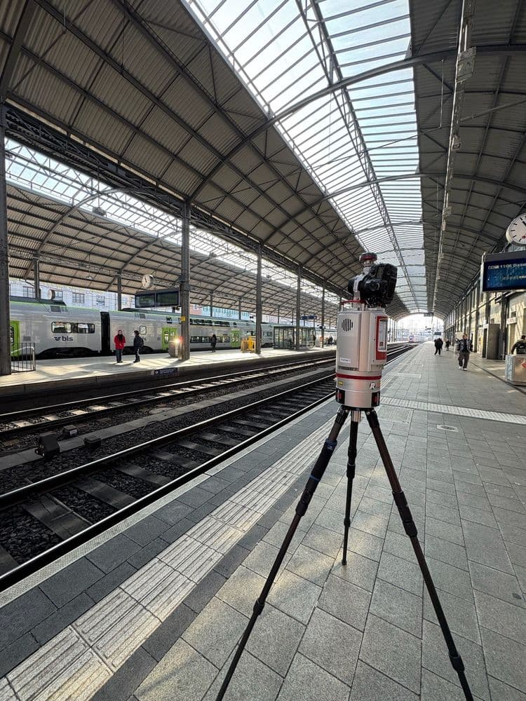 Moderne Bahnhofshalle mit hohen Glasdächern, Dreibein-Stativ im Vordergrund.