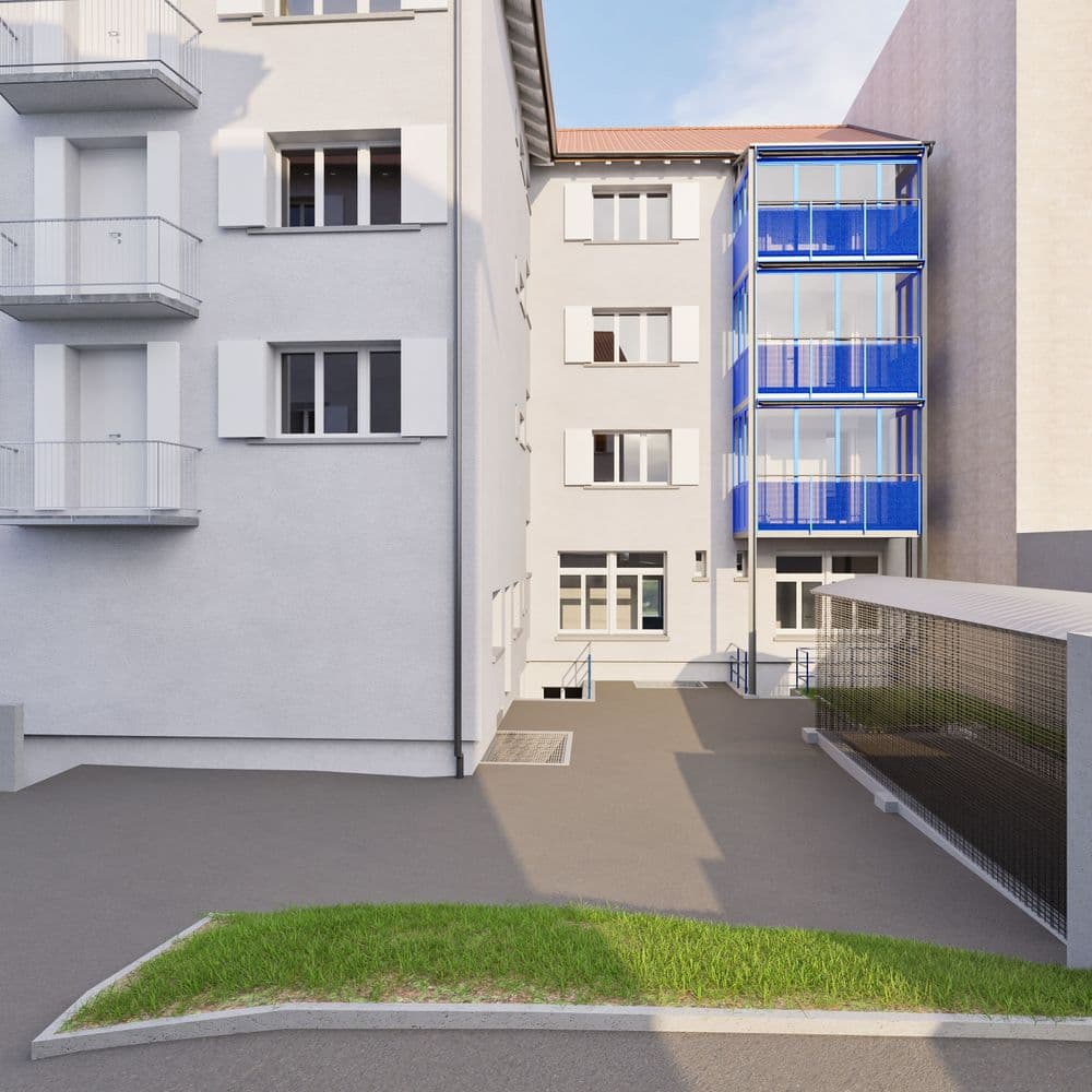 Mehrfamilienhaus mit modernem, blau verglastem Anbau und grünem Vorgarten.