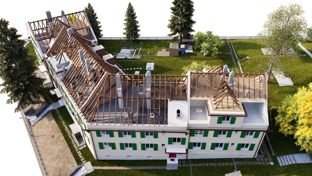 3D-Visualisierung einer Baustelle: Mehrstöckiges Gebäude mit geöffnetem Dachstuhl und Holzsparren, teils ohne Dachdeckung, von oben; grünes Umfeld mit Bäumen und Wegen.
