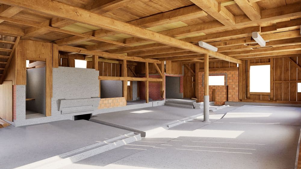 Innenraum eines Gebäudes im Rohbau: Holztragwerk mit Deckenbalken, Betonboden, gemauerte Wände und Fensteröffnungen, Baustellenansicht in hellem Tageslicht.