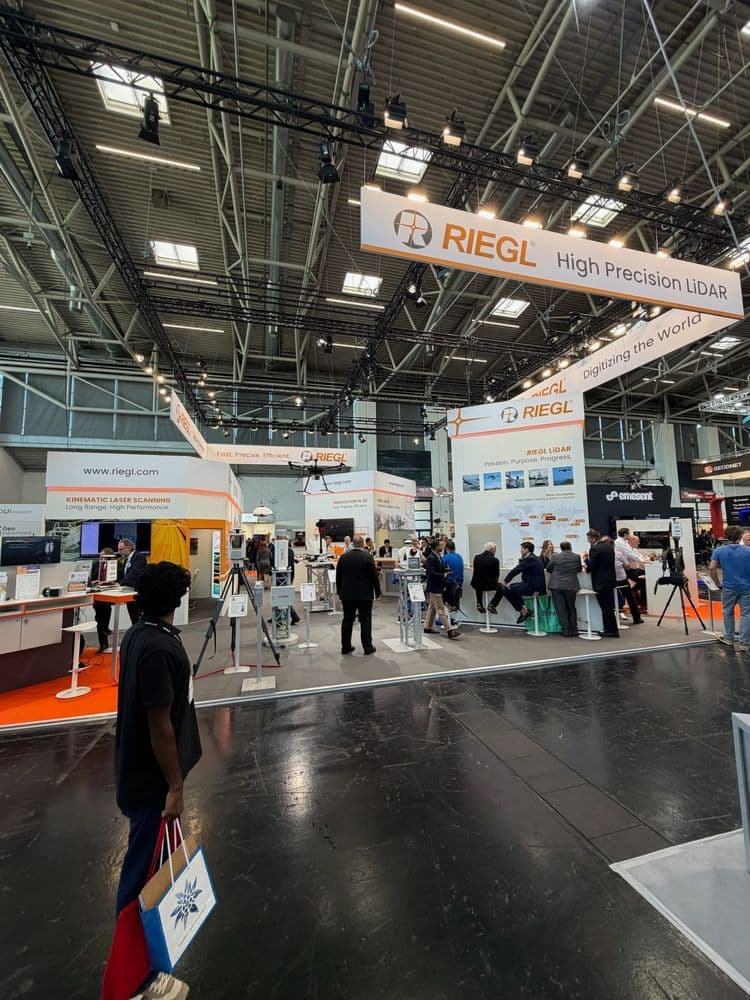 Messestand von RIEGL auf einer Fachmesse: High Precision LiDAR, Besucher an Ständen, Hallendecke mit Lichttraversen, Präsentationsflächen und Displays.