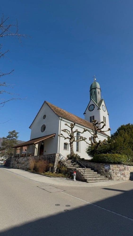 Kirche in Büsserach mit Glockenturm, blauer Himmel im Hintergrund.
