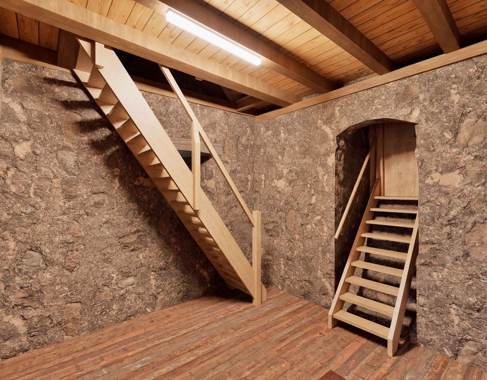 Holztreppe in einem rustikalen Raum mit Steinwänden und Holzbalkendecke.
