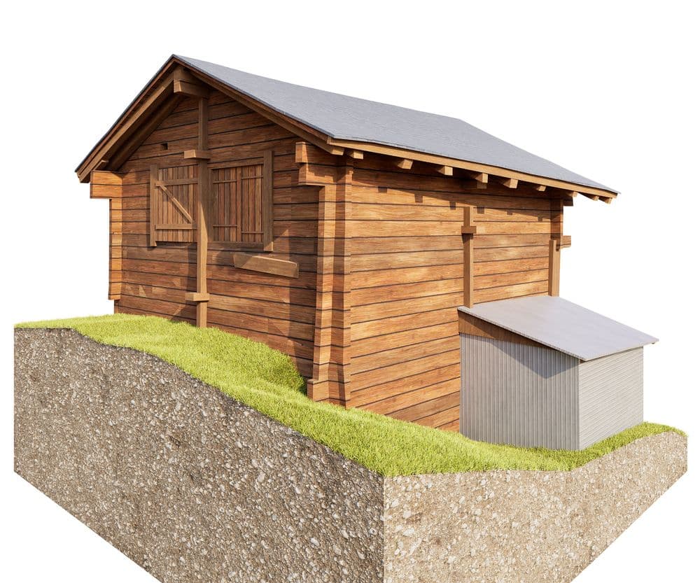 3D-Illustration eines Holzschuppens mit Satteldach auf grasbewachsenem Erdquerschnitt, daneben kleiner grauer Anbau; Gartenhaus/Lagerschuppen aus Holz auf weißem Hintergrund.