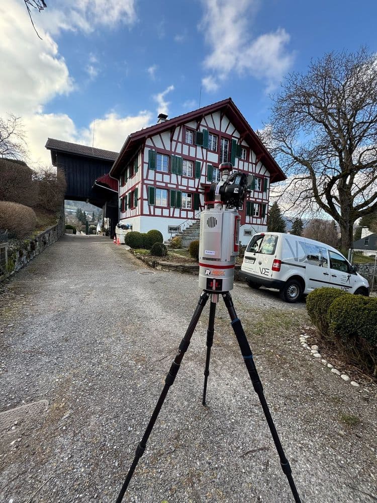 Dreibein-Stativ mit Laserscanner vor einem traditionellen Fachwerkhaus und einem geparkten Lieferwagen.