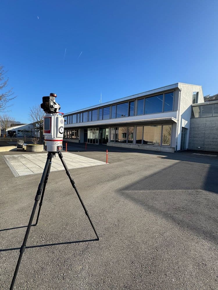 Ein Hochpräzisions-3D-Scanner auf einem Stativ steht vor einem modernen Gebäude bei sonnigem Wetter.