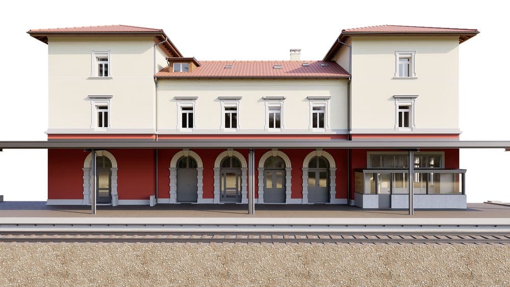 Frontansicht eines historischen Bahnhofsgebäudes mit roten Ziegelarkaden, beigem Obergeschoss, roten Ziegeldächern und Bahnsteigüberdachung, freigestellt auf weißem Hintergrund.