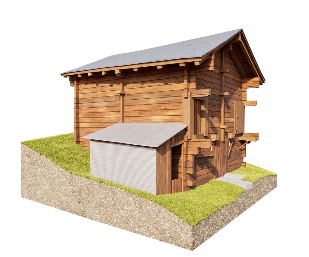 3D-Rendering eines traditionellen Holzhauses mit Satteldach auf einem Erd- und Grasquerschnitt, mit angebautem kleinen Schuppen oder Garagenanbau, freigestellt vor weißem Hintergrund.