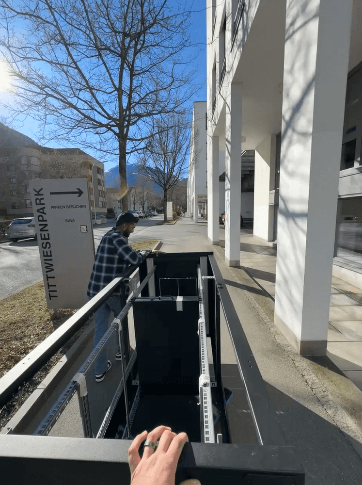 Ein Mann bewegt einen Wagen auf einem Gehweg in einer modernen Stadtumgebung neben einem Schild mit der Aufschrift "Tittwiesenpark".