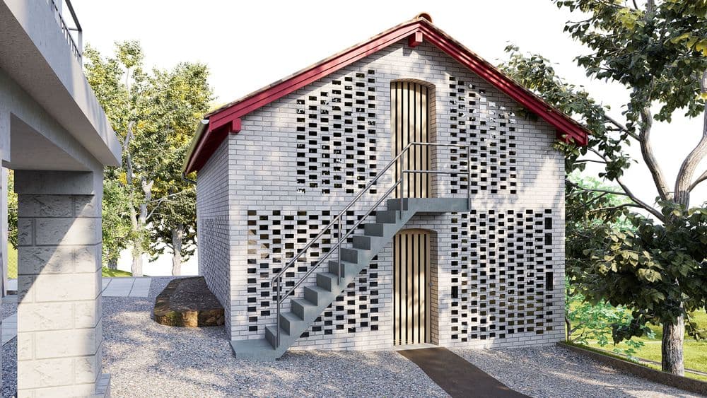 3D-Visualisierung eines kleinen grauen Backsteinhauses mit roten Dachkanten, Außentreppe zu einer oberen Tür, Lochmuster-Mauerwerk, Bäumen und Kieshof im Tageslicht.