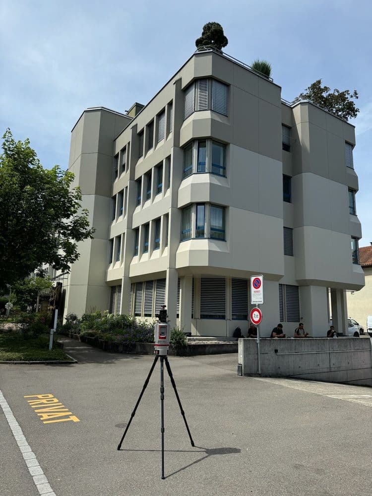 Modernes Mehrfamilienhaus mit Balkonen und Vermessungsstativ vorne.